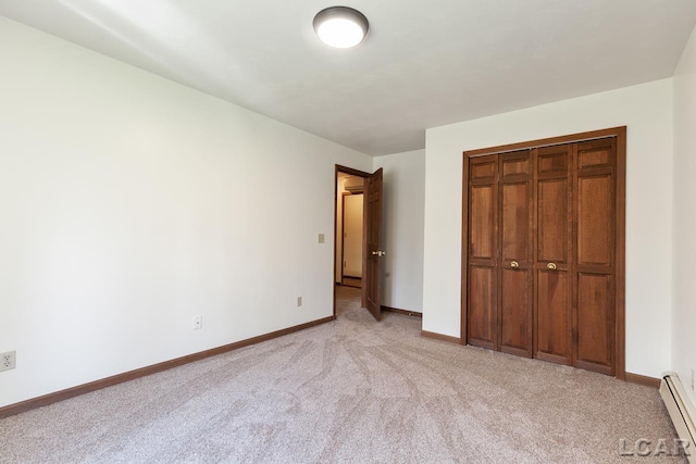 unfurnished bedroom featuring a baseboard heating unit, light carpet, and a closet