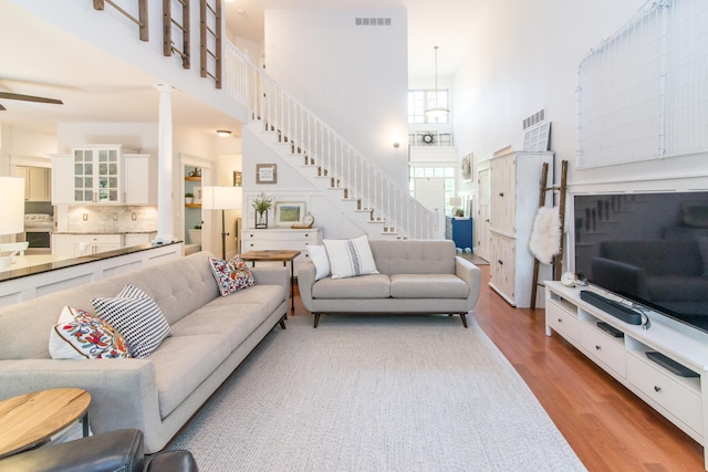 living room with ceiling fan, light hardwood / wood-style floors, ornate columns, and a high ceiling