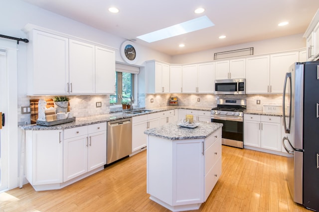 kitchen featuring a skylight, white cabinetry, a kitchen island, and appliances with stainless steel finishes