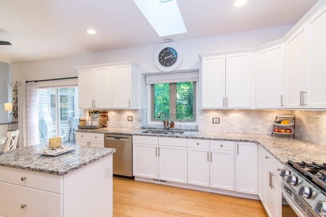 kitchen with a skylight, white cabinetry, sink, stainless steel appliances, and light hardwood / wood-style floors