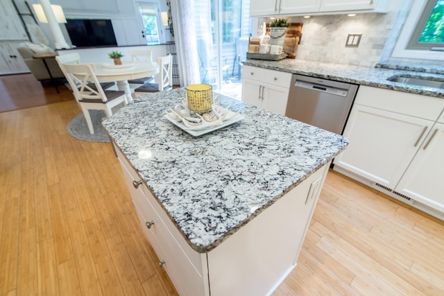 kitchen with white cabinets, stainless steel dishwasher, light stone counters, and light hardwood / wood-style flooring