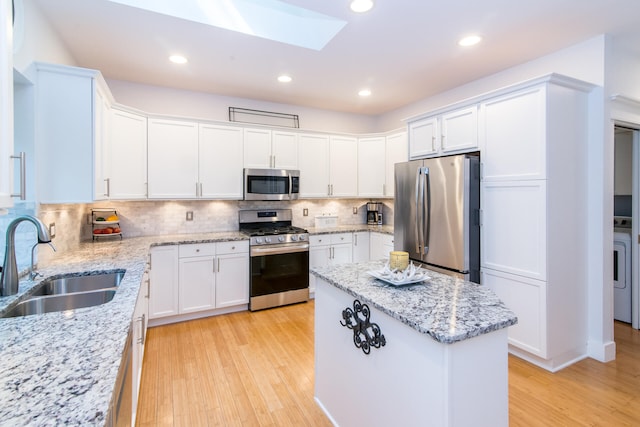 kitchen with white cabinets, sink, a skylight, light wood-type flooring, and appliances with stainless steel finishes