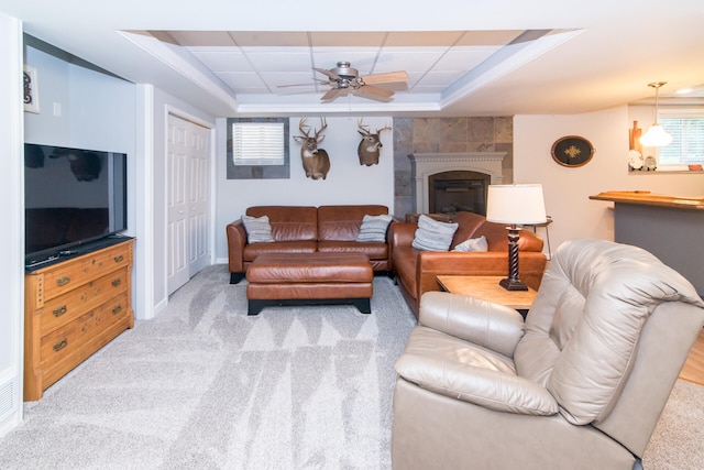 carpeted living room featuring a tray ceiling, ceiling fan, and a fireplace