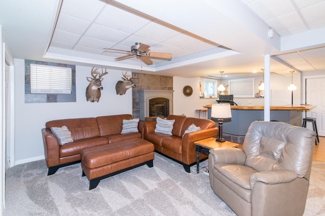 living room featuring a tray ceiling, a tile fireplace, ceiling fan, and light carpet