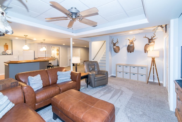 living room featuring a tray ceiling, ceiling fan, crown molding, and light colored carpet