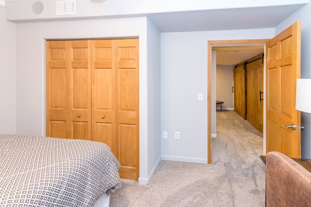 bedroom with a barn door, light colored carpet, and a closet