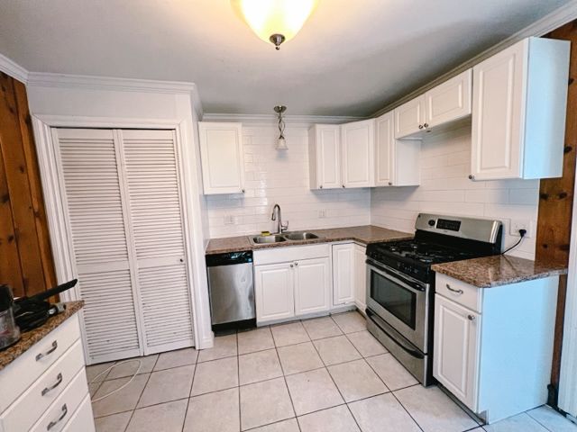 kitchen featuring tasteful backsplash, appliances with stainless steel finishes, dark stone countertops, white cabinetry, and a sink