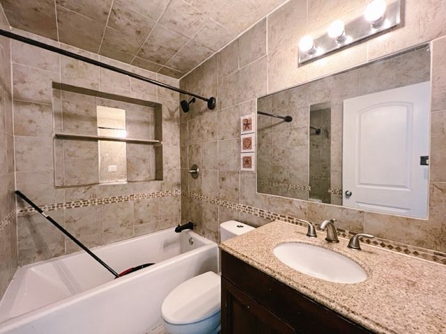 bathroom featuring tile walls, toilet, vanity, washtub / shower combination, and backsplash