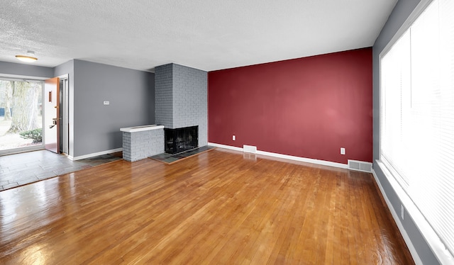 unfurnished living room featuring hardwood / wood-style flooring, a textured ceiling, and a brick fireplace