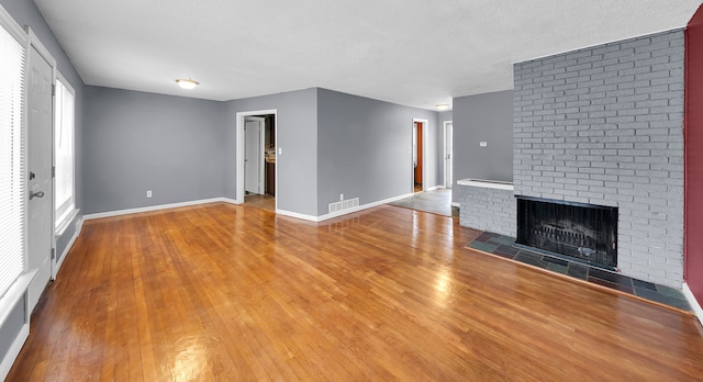 unfurnished living room with wood-type flooring, a textured ceiling, and a brick fireplace