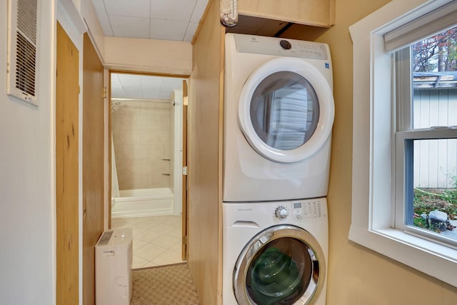 laundry room with tile patterned flooring, stacked washer / drying machine, and a wealth of natural light