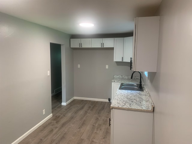 kitchen with light stone countertops, wood-type flooring, white cabinetry, and sink