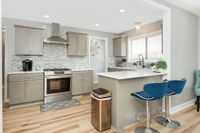 kitchen with sink, wall chimney exhaust hood, tasteful backsplash, stainless steel range with gas stovetop, and light wood-type flooring