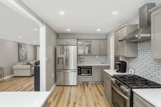 kitchen with gray cabinetry, wall chimney exhaust hood, decorative backsplash, light hardwood / wood-style floors, and stainless steel appliances