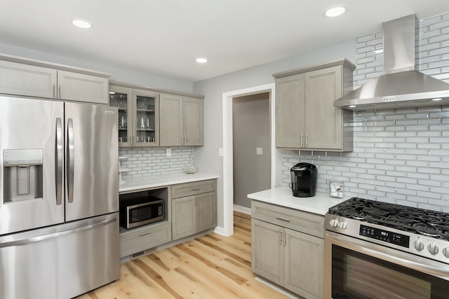 kitchen with backsplash, stainless steel appliances, light hardwood / wood-style flooring, and wall chimney range hood