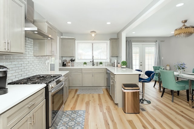 kitchen with a kitchen bar, backsplash, stainless steel appliances, wall chimney range hood, and light hardwood / wood-style floors