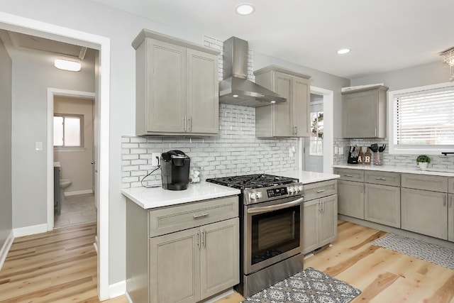 kitchen featuring gray cabinetry, wall chimney range hood, light wood-type flooring, tasteful backsplash, and gas stove