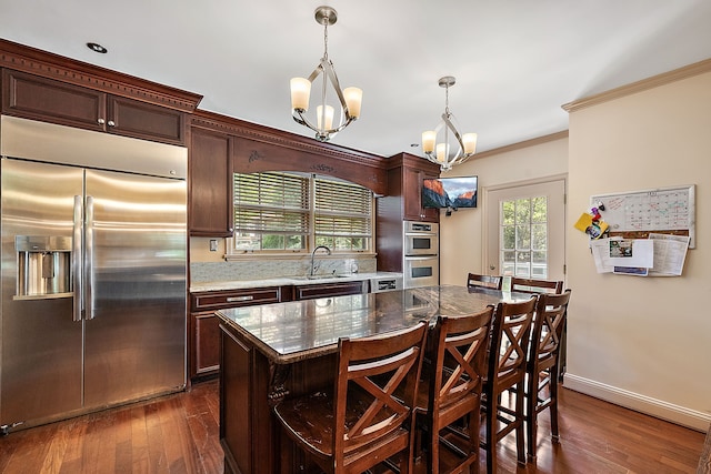 kitchen with dark wood-type flooring, a chandelier, decorative light fixtures, a kitchen island, and appliances with stainless steel finishes