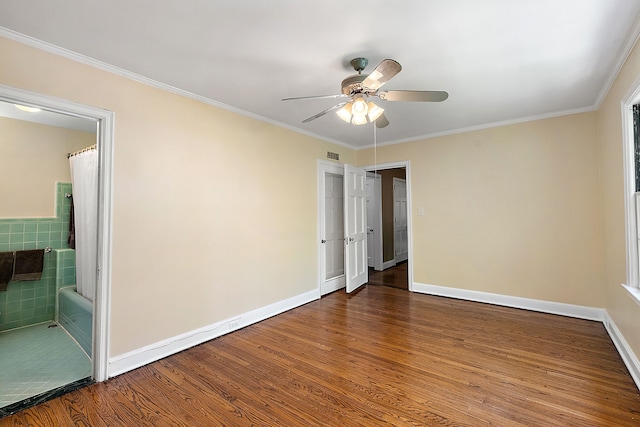 empty room with hardwood / wood-style flooring, ceiling fan, crown molding, and tile walls