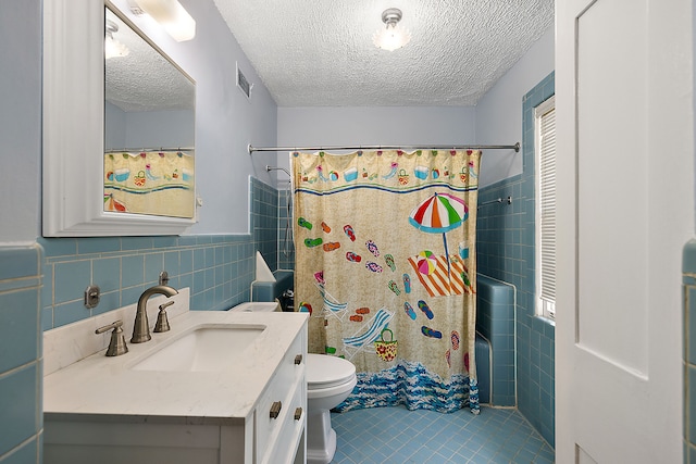 full bathroom featuring tile patterned floors, vanity, a textured ceiling, tile walls, and toilet