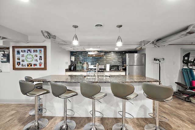 kitchen featuring pendant lighting, stainless steel fridge, dark stone countertops, and sink