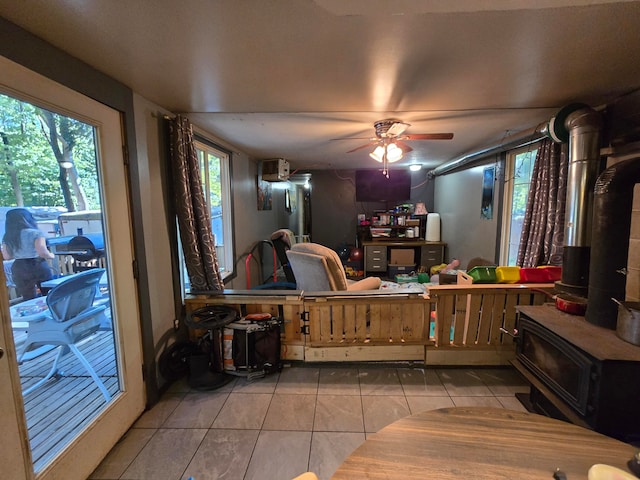 tiled living room featuring a wood stove, ceiling fan, and plenty of natural light