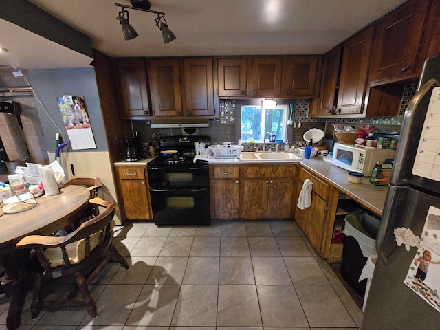 kitchen with stainless steel fridge, backsplash, black range with electric cooktop, sink, and light tile patterned floors