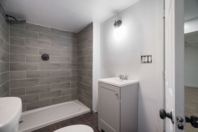 bathroom with toilet, hardwood / wood-style floors, vanity, and tiled shower