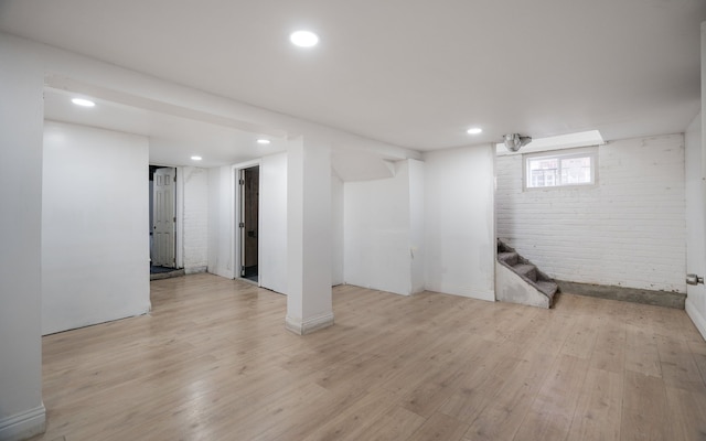 basement with light hardwood / wood-style floors and brick wall