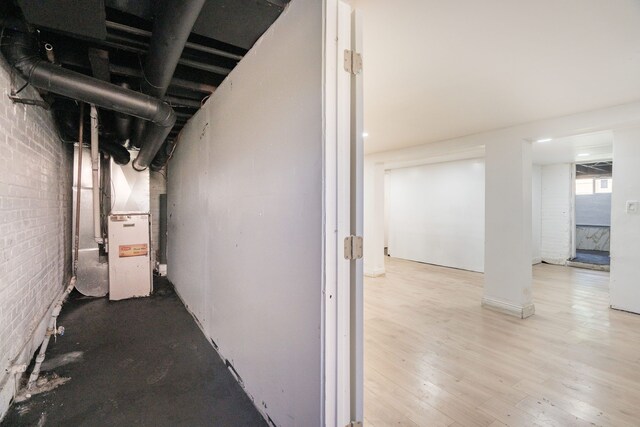 basement with light wood-type flooring, heating unit, and brick wall