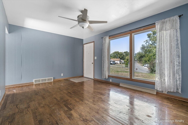 unfurnished room featuring hardwood / wood-style flooring, ceiling fan, wood walls, and baseboard heating