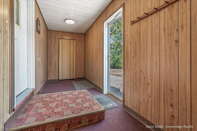 entryway with wooden walls and dark colored carpet