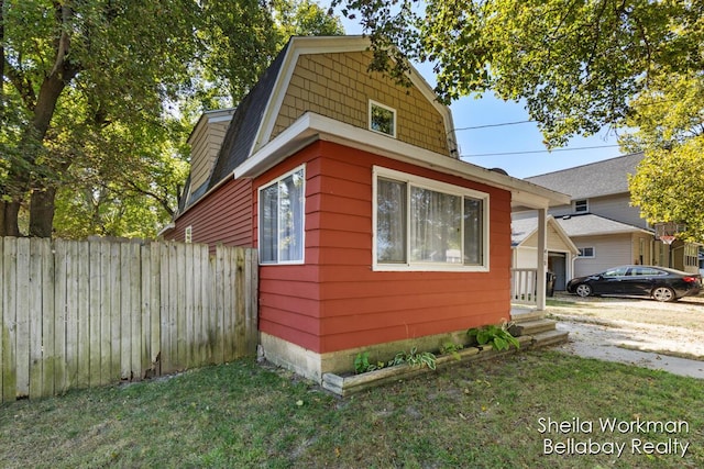 view of side of home featuring a yard, fence, and a gambrel roof