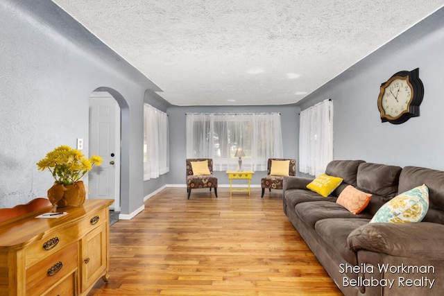 living room with light wood-type flooring, baseboards, arched walkways, and a textured ceiling