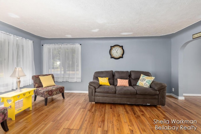 living area with arched walkways, baseboards, a textured ceiling, and hardwood / wood-style floors