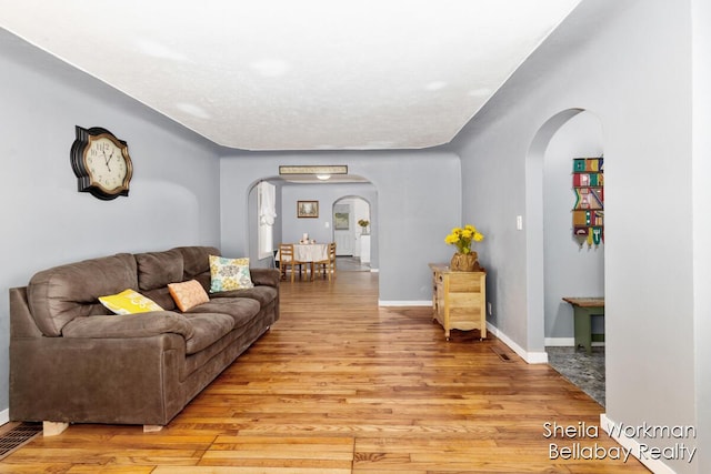 living room featuring arched walkways, light wood-style flooring, and baseboards