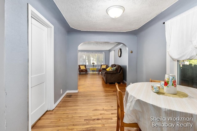 dining room with arched walkways, a textured ceiling, light wood-type flooring, and baseboards