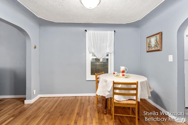 dining space with arched walkways, a textured ceiling, hardwood / wood-style flooring, and baseboards