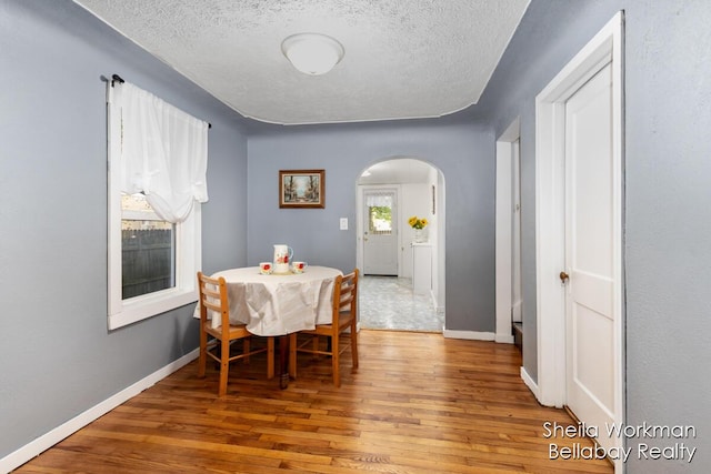 dining room with arched walkways, a textured ceiling, baseboards, and wood finished floors