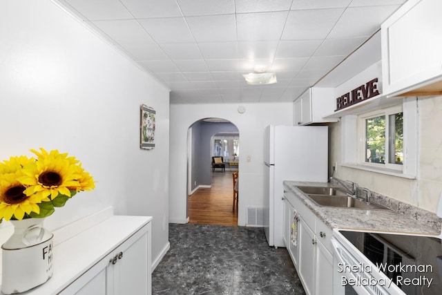 kitchen with white appliances, arched walkways, white cabinets, and a sink