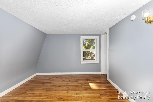 unfurnished room featuring a textured ceiling, baseboards, vaulted ceiling, and wood finished floors