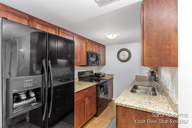 kitchen featuring black appliances, light hardwood / wood-style floors, light stone counters, and sink