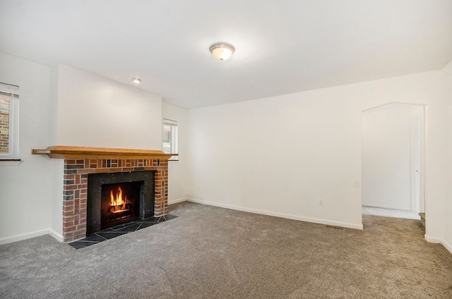 unfurnished living room with dark colored carpet, a brick fireplace, and a wealth of natural light