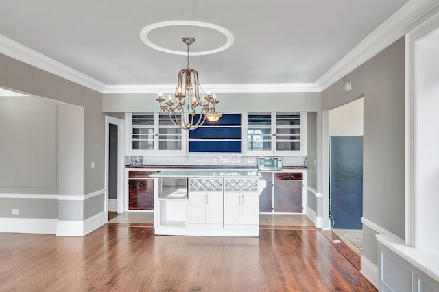 kitchen with hardwood / wood-style floors, pendant lighting, crown molding, tasteful backsplash, and a notable chandelier