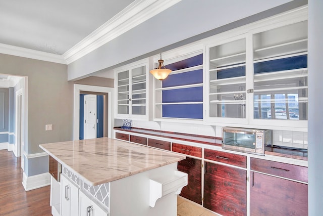 kitchen featuring light stone counters, ornamental molding, hardwood / wood-style flooring, a center island, and hanging light fixtures