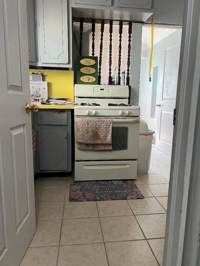 kitchen with gray cabinets, light tile patterned floors, and white gas range oven