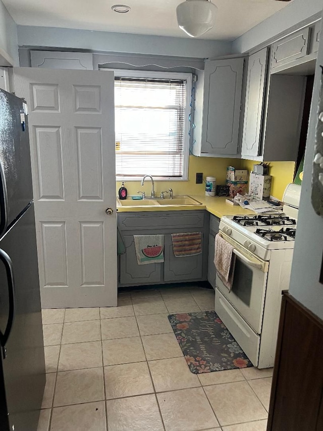 kitchen with stainless steel refrigerator, white gas stove, sink, gray cabinets, and light tile patterned flooring