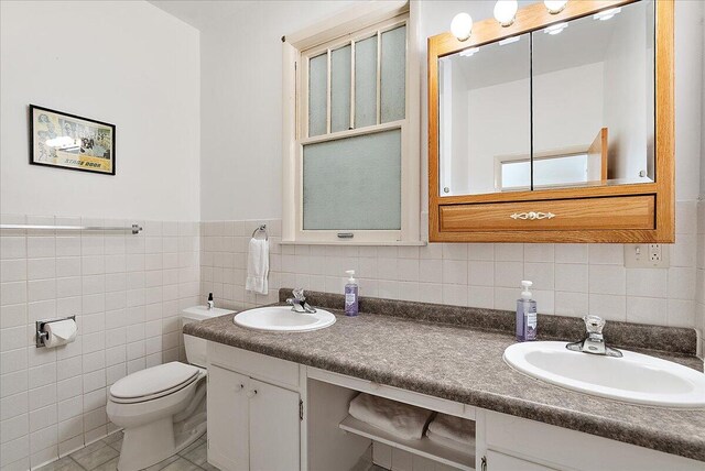 full bathroom with double vanity, tile walls, toilet, and a sink