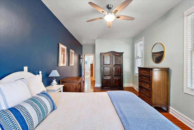 bedroom featuring multiple windows, dark wood finished floors, a ceiling fan, and baseboards