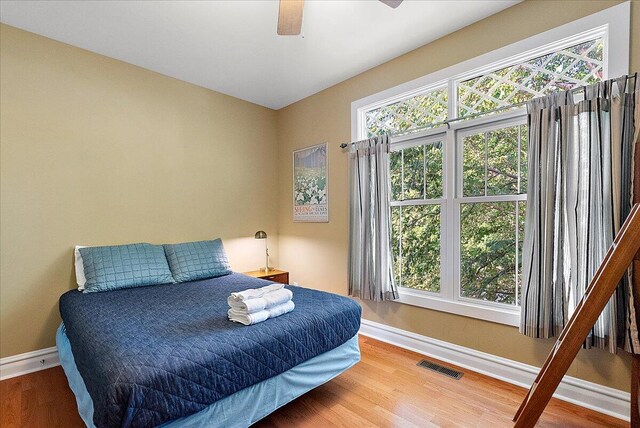 bedroom with multiple windows, wood finished floors, visible vents, and baseboards